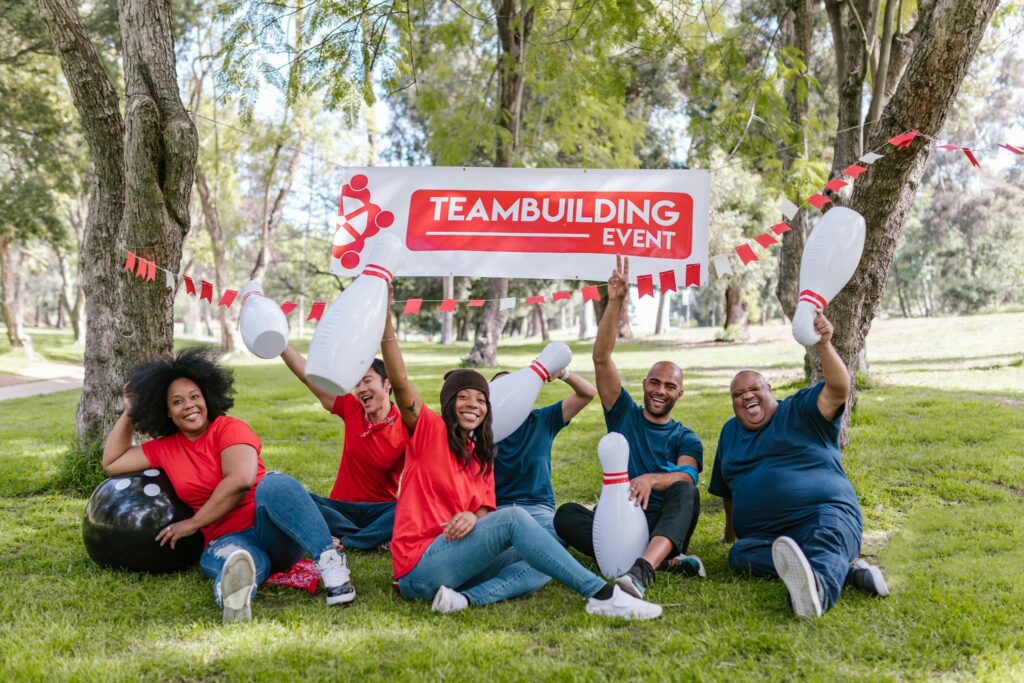 Cheerful group of diverse adults enjoy a team building event outdoors with bowling props.